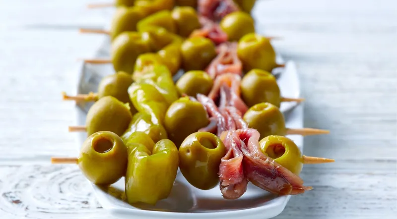 A white plate of gilda skewers with olives and anchovies