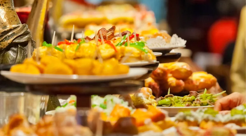 A crowded pintxos counter in the San Sebastian Old Town, plates stacked on tiered stands