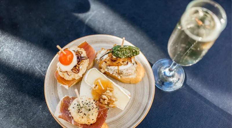 A plate of four assorted pintxos beside a glass of sparkling wine, seen from above