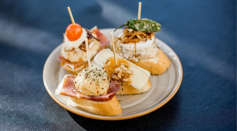 A plate of jamon and cheese pintxos on a dark table at an evening pintxos tour in San Sebastian