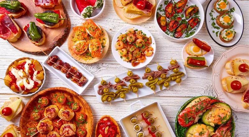 A large spread of Spanish tapas dishes laid out on a white wooden table